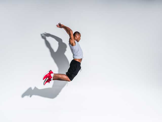 side view of young african american sportsman jumping on grey